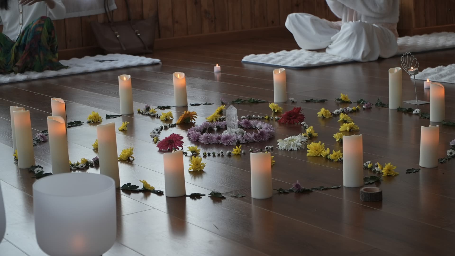 A floral and candle altar laid out on the floor with a crystal at its centre
