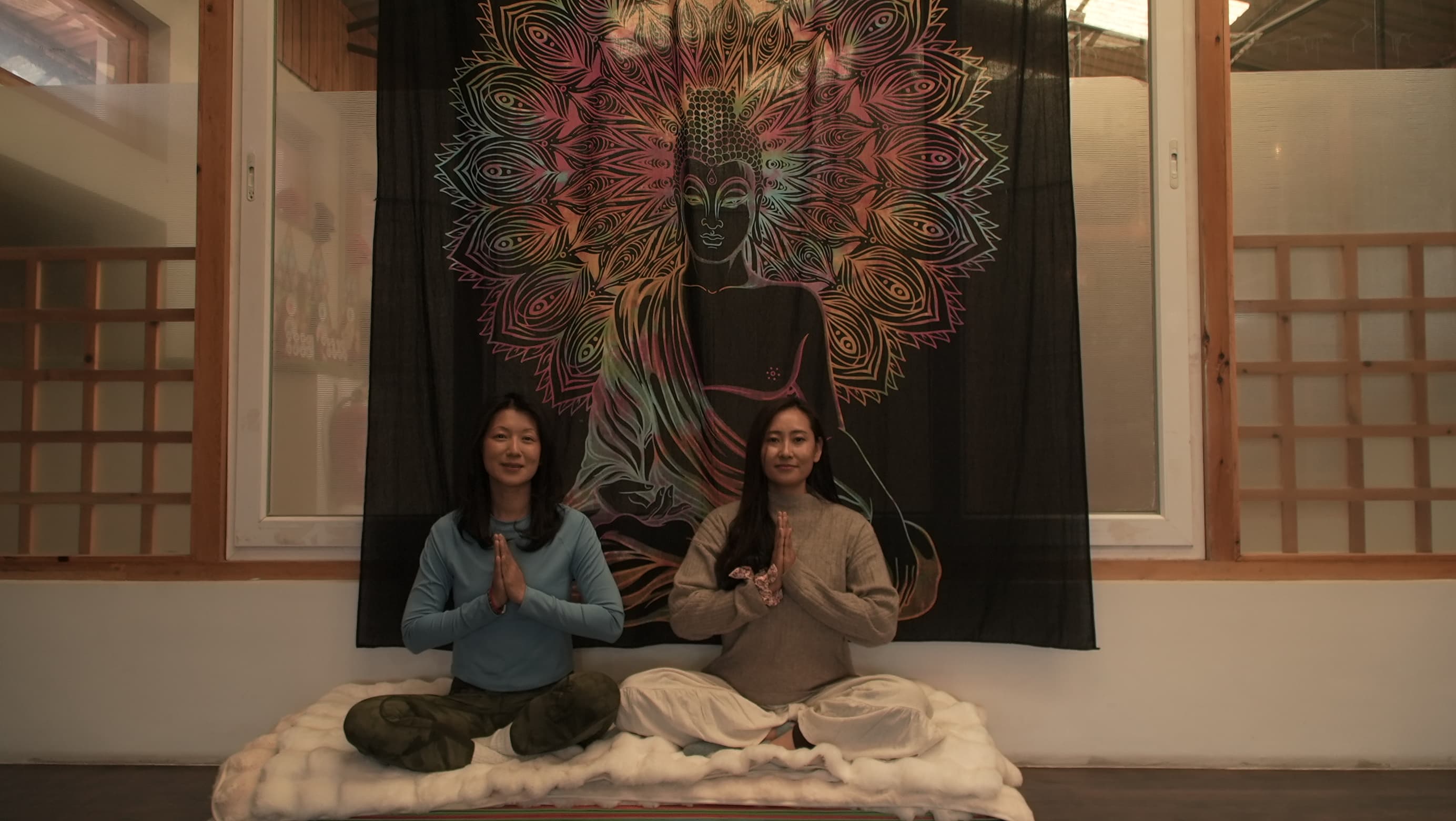 Tshering and Jigme seated in prayer before a Buddha tapestry