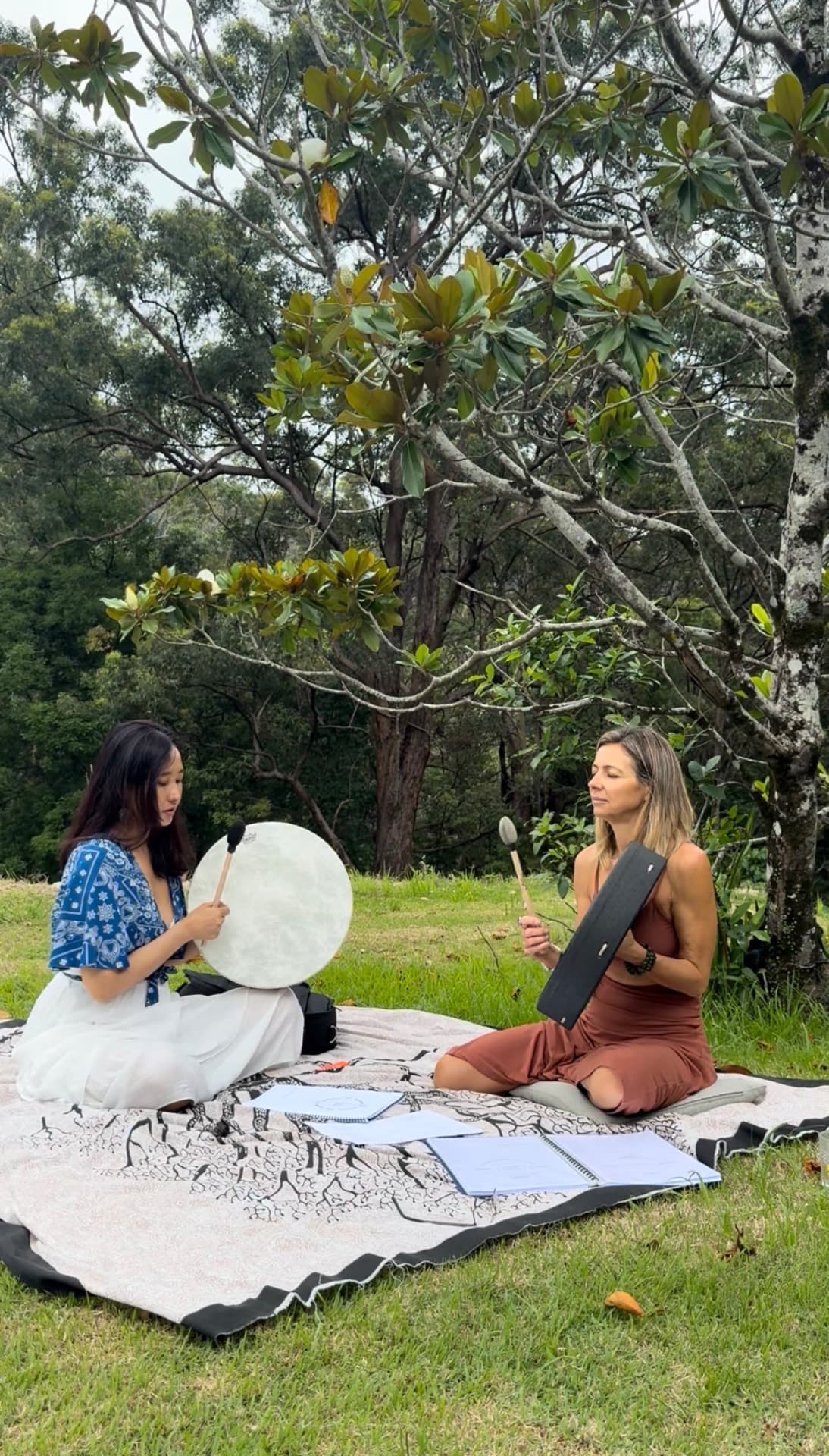 Tshering playing a frame drum outdoors under a tree